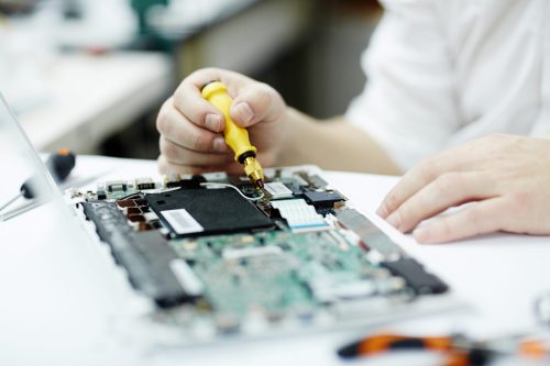 Closeup shot of unrecognizable man assembling circuit board in laptop using screwdriver and different tools on table in workshop